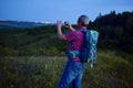 Active middle aged man standing on hill with backpack, taking picture of mountains landscape during twilight. Man taking picture Royalty Free Stock Photo