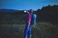 Active middle aged man standing on hill with backpack, taking picture of mountains landscape during twilight. Man taking picture Royalty Free Stock Photo