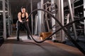 Active motivated sportswoman training in the gym with battle ropes, determined confident girl enjoying bodybuilding, a