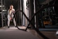 Active motivated sportswoman trains in the gym with battle ropes, determined confident girl enjoys bodybuilding, doing