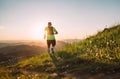 Active mountain trail runner dressed bright t-shirt with backpack running endurance marathon race by picturesque hills at sunset