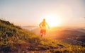 Active mountain trail runner dressed bright t-shirt with backpack running endurance marathon race by picturesque hills at sunset