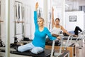 Mature woman in sportswear sitting and doing Pilates exercises for hands on reformer bed equipment in fitness center Royalty Free Stock Photo