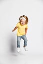 Active playful kid baby girl blonde in yellow t-shirt, blue jeans and sneakers is jumping high, having fun, flying