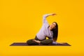 Active pregnancy concept. Happy future mom doing her morning yoga workout on mat over yellow studio background Royalty Free Stock Photo