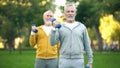 Active retired friends lifting dumbbells, fitness training park, healthy aging