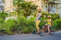 Active school kid boy and his mom in medical mask and safety helmet riding a bike with backpack on sunny day. Happy