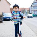 Active school kid boy in safety helmet riding with his scooter in the city with backpack on sunny day. Happy child in