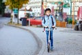 Active school kid boy in safety helmet riding with his scooter in the city with backpack on sunny day. Happy child in