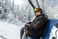 Active senior experienced mature old person in ski helmet, goggles and black suit sit resting on ski lift mountain peak