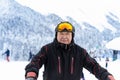 Active senior experienced mature old person in ski helmet, goggles and black suit stand against scenic panorama peak