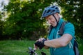 Active senior man riding bicycle at summer park, looking at smartwatch and checking his performance, healthy lifestyle Royalty Free Stock Photo