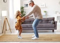 Active senior grandfather enjoying dance with cute little granddaughter in living room at home