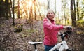 Active senior woman with bicycle standing outdoors in nature.