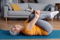 Active senior woman doing exercises on yoga mat, working out at home, relaxing her back muscles Royalty Free Stock Photo