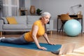 Active senior woman doing sphinx cobra pose or upward-facing dog asana, excercising on mat and using laptop Royalty Free Stock Photo