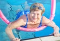 Senior woman (over age of 50) in sport goggles, swimsuit doing aqua fitness with swim noodles in swimming pool. Royalty Free Stock Photo