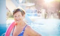 Active senior woman (over age of 50) in sport goggles, swimsuit, with swim noodles near swimming pool. Royalty Free Stock Photo