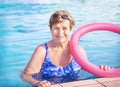 Active senior woman (over age of 50) in sport goggles, swimsuit, with swim noodles in swimming pool. Royalty Free Stock Photo