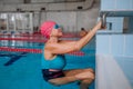 Active senior woman swimmer holding onto starting block preparing to swim in indoors swimming pool. Royalty Free Stock Photo