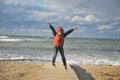 Active small boy in red and blue jacket and hood jumping near stormy sea in autumn weather sunset leisure Royalty Free Stock Photo