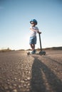 Active small kid in helmet and sunglasses with scooter on empty old highway