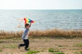 Active small kid running with colorful kite in his hand on sea shore background outdoor leisure games