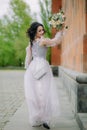 Active smiling bridesmaid with elegant dress standing next to the church and showing bridal bouquet