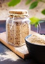 Active sourdough starter in glass jar. Rye leaven for bread and cup of flour on wooden cutting board on black and brown rustic