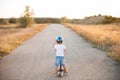 Active sport little child in helmet and denim shorts standing on desert road with scooter on summer warm sunset Royalty Free Stock Photo