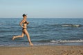 Active sporty woman run along ocean surf by water pool to keep fit and health. Sunset black sand beach background with Royalty Free Stock Photo