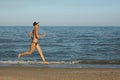 Active sporty woman run along ocean surf by water pool to keep fit and health. Sunset black sand beach background with Royalty Free Stock Photo