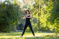 Active and sporty young woman standing in the park on a mat in a pose, doing morning exercises and yoga Royalty Free Stock Photo