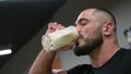 active strong young bearded male athlete drinking milk protein gainer from glass indoors