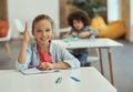 Active student. Cute little school girl smiling at camera raised her hand while sitting at the desk in classroom Royalty Free Stock Photo