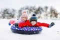 Active toddler girl and school boy sliding together down the hill on snow tube. Happy children, siblings having fun Royalty Free Stock Photo