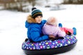 Active toddler girl and school boy sliding together down the hill on snow tube. Happy children, siblings having fun Royalty Free Stock Photo