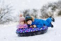 Active toddler girl and school boy sliding together down the hill on snow tube. Happy children, siblings having fun Royalty Free Stock Photo