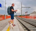 Active tourist with backpack using phone and waiting for train. Man and beagle dog waiting on railway station. Older Royalty Free Stock Photo