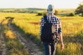 Active tourist, a man with a briefcase in nature, a hipster in a cap is walking along a path on a green hill, healthy lifestyle