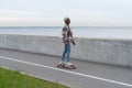 Active urban lifestyle: african girl riding longboard at seaside road. Smiling woman on skateboard