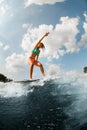 active woman in colorful swimsuit energetically balancing on wave on wakesurf board.
