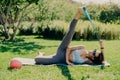 Active woman does workout outside. Slim brunette woman stretches legs with sports gum dressed in activewear lying on fitness mat