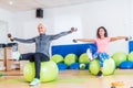 Active women sitting on exercise balls lifting legs and doing dumbbell lateral raise. Two mature females working out in