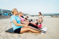 Active women of various ages doing fitness workouts in class exercise with coach on the beach. Ladies working with