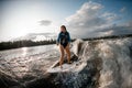 Active young brown-haired woman wakesurfing down the river waves