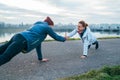 Active young Caucasian couple in athletic jackets and beanies performing high plank variations while giving each other a high-five Royalty Free Stock Photo