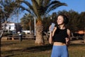 Active young fit woman in wireless headphones drinks water from bottle after exercising outdoors at palm trees park Royalty Free Stock Photo