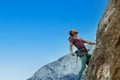 Active young man climbing on height vertical rock against blue sky. climber looking up and overcoming a difficult route Royalty Free Stock Photo