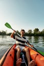 Active young man looking cheerful while kayaking in a lake, surrounded by peaceful nature on a summer afternoon
